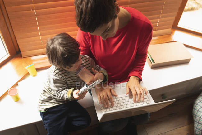 Вид с воздуха на мать и сына, сидящих с ноутбуком дома — стоковое фото