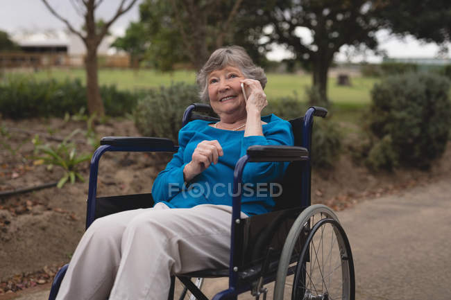 Щаслива старша жінка на кріслі розмовляє на мобільному телефоні — стокове фото