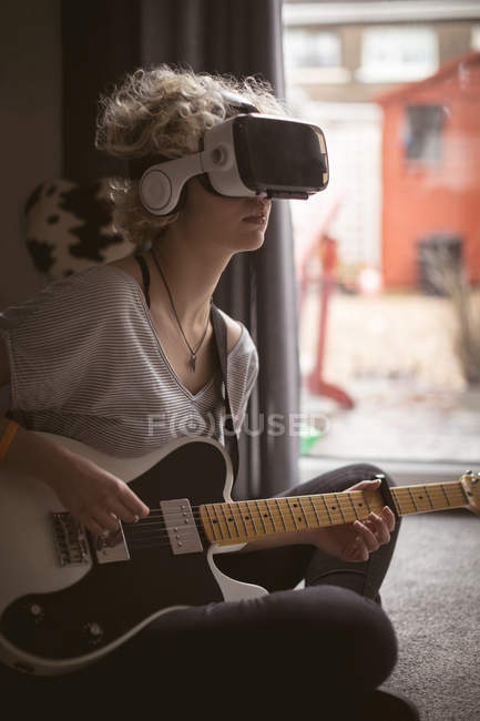 Junge Frau benutzt virtuelles Headset, während sie zu Hause Gitarre spielt — Stockfoto