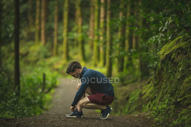 Apto homem amarrando seu cadarço na floresta — Fotografia de Stock