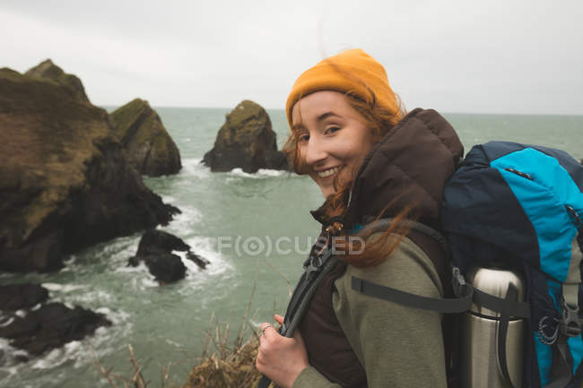 Portrait d'une randonneuse souriante debout au bord de la mer et regardant la caméra — Photo de stock