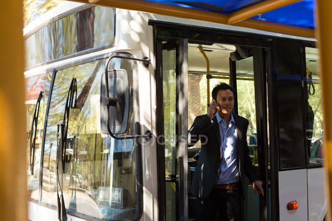 Чоловік розмовляє по мобільному телефону, виходячи з автобуса — стокове фото