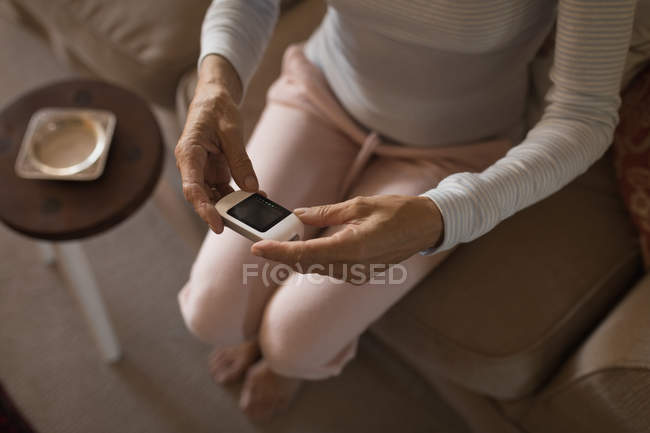 Sezione bassa della donna anziana che controlla il misuratore di glucosio a casa — Foto stock
