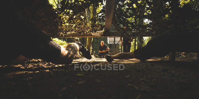 Подходящие мужчины ползают под сетью во время полосы препятствий в учебном лагере — стоковое фото