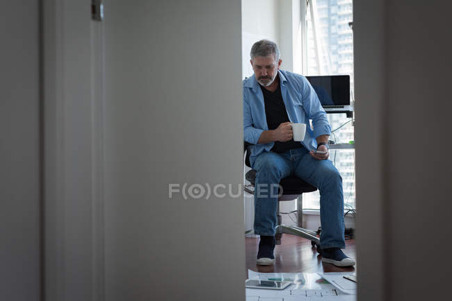 Homem maduro tomando café enquanto trabalhava em casa — Fotografia de Stock