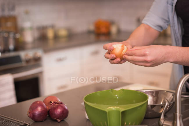 Woman removing peel of onion in kitchen at home — Stock Photo