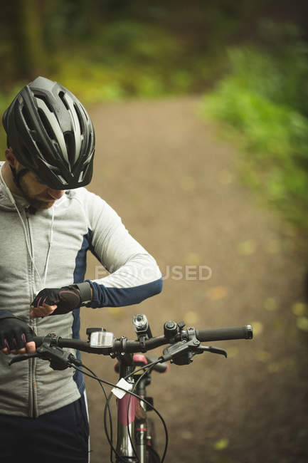 Ciclista verificando o tempo em smartwatch na floresta — Fotografia de Stock