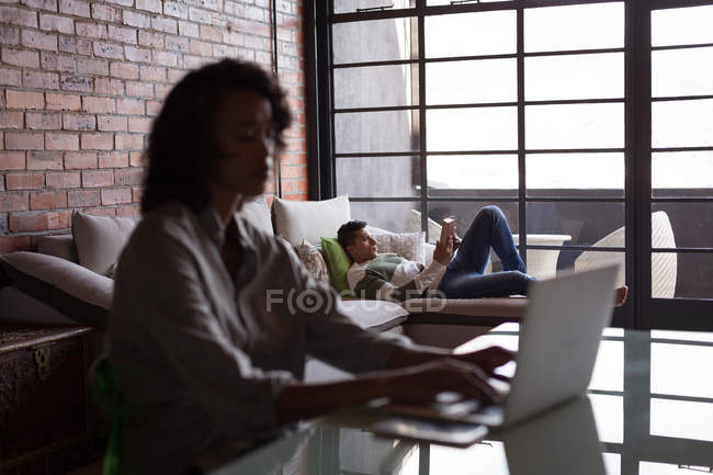 Mulher usando laptop enquanto homem lendo um livro em casa — Fotografia de Stock
