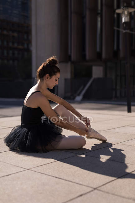 Dançarina de ballet feminina amarrando a fita em seus sapatos de balé na cidade — Fotografia de Stock