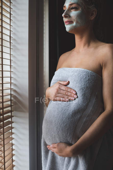 Femme enceinte avec crème faciale dans la salle de bain à la maison — Photo de stock