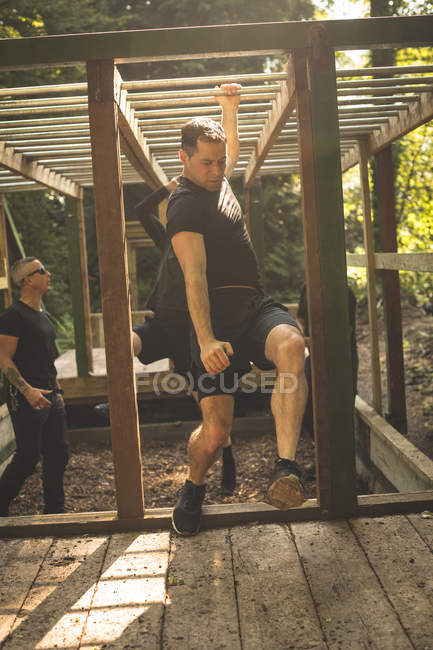 Fit man climbing monkey bars at boot camp — Stock Photo