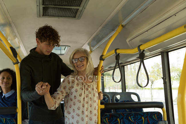 Hombre joven ayudando a la mujer mayor mientras viaja en el autobús - foto de stock