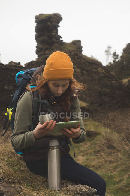 Senderista femenina concentrada leyendo un mapa y tomando una copa - foto de stock