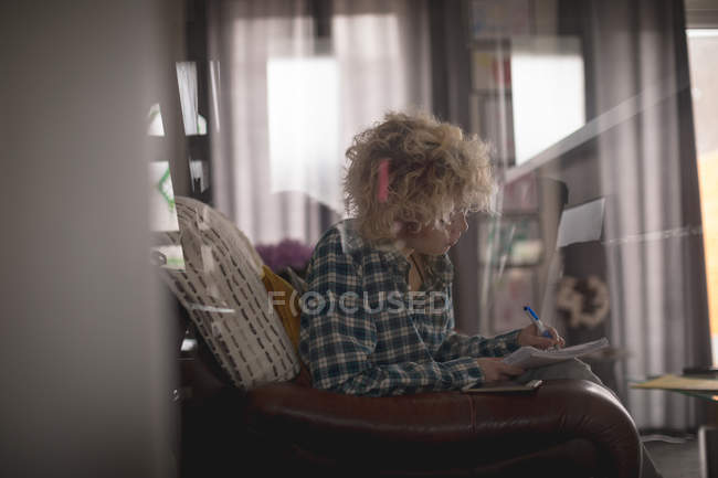 Blogger mujer escribiendo en un bloc de notas en la sala de estar en casa - foto de stock