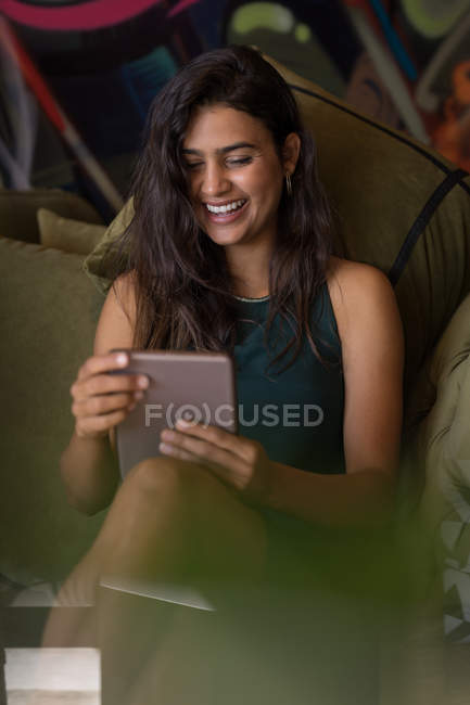 Donna d'affari seduta sul divano e sorridente durante l'utilizzo di tablet in ufficio — Foto stock