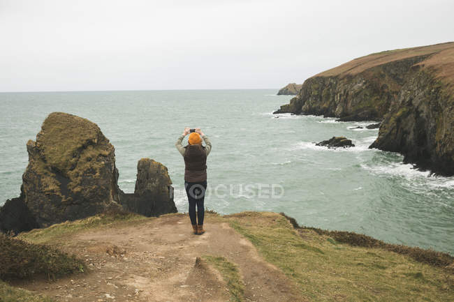 Visão traseira do caminhante feminino fotografando o mar — Fotografia de Stock