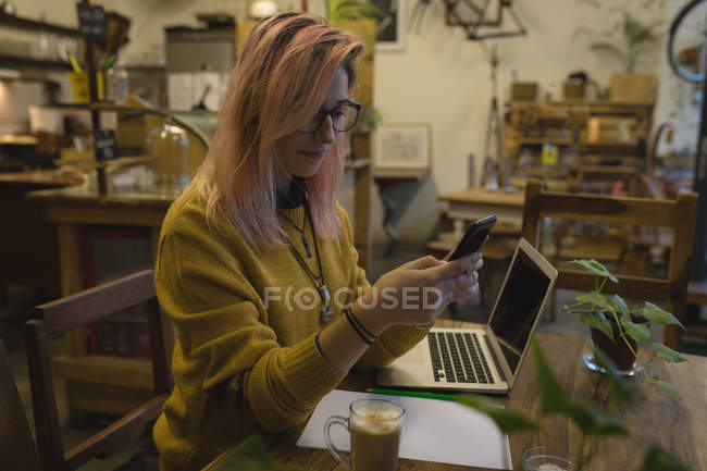 Mujer joven usando un teléfono móvil en la cafetería - foto de stock