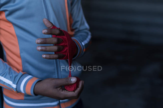 Mid section of male boxer tying hand wrap on hand in fitness studio — Stock Photo