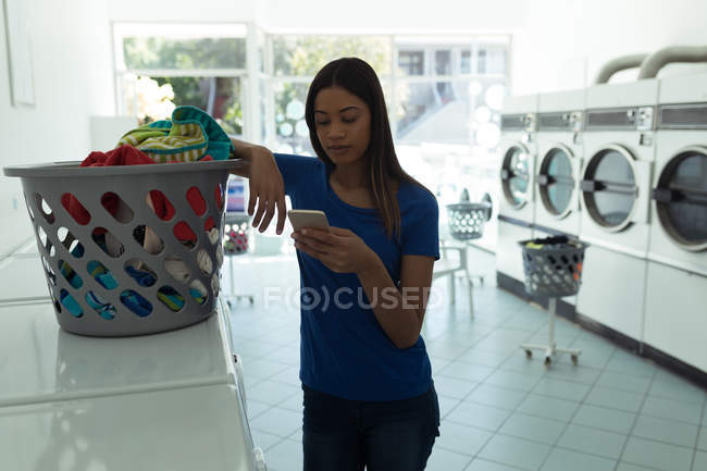 Young woman using phone at laundromat — Stock Photo