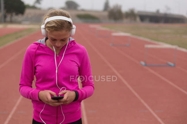 Atleta femminile che ascolta musica sul cellulare in pista — Foto stock