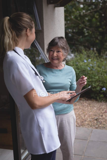 Fisioterapeuta e mulher idosa usando um comprimido em casa — Fotografia de Stock