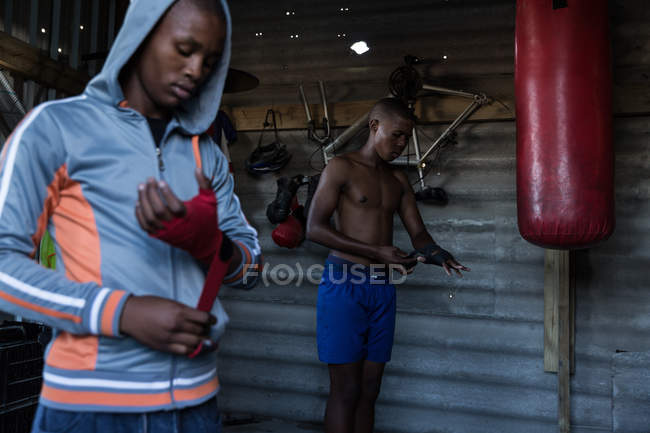 Boxeador masculino atando envoltura de mano en la mano en el gimnasio - foto de stock