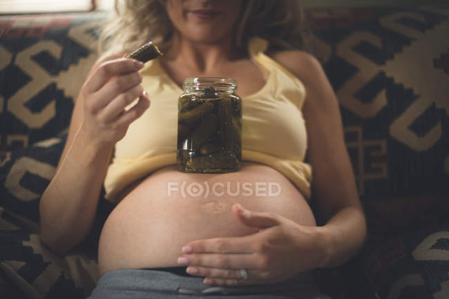 Беременная женщина с огурцом в гостиной дома — стоковое фото