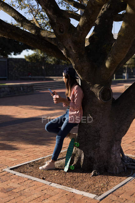Mujer apoyada contra un árbol en el parque - foto de stock