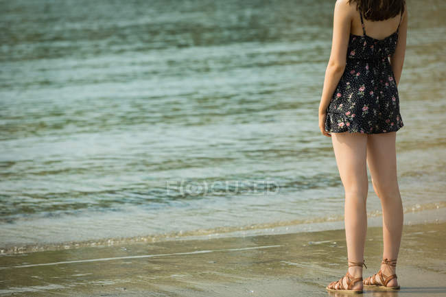 Вид сзади на женщину, стоящую на пляже в солнечный день — стоковое фото