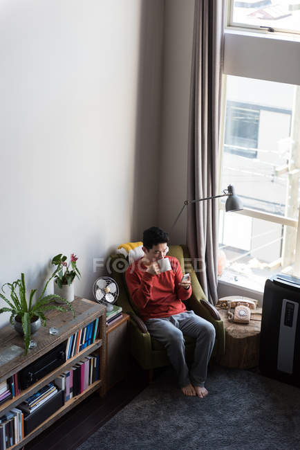 Man having coffee while using mobile phone in living room at home — Stock Photo
