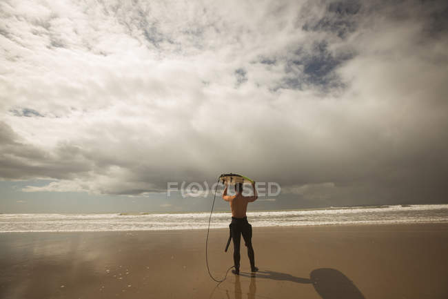 Surfeur portant la planche de surf sur sa tête par une journée ensoleillée — Photo de stock