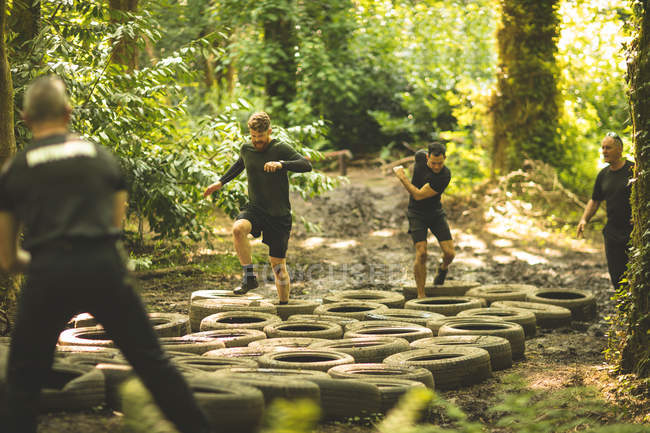 Homens aptos a treinar sobre pneus curso de obstáculo no acampamento de inicialização — Fotografia de Stock