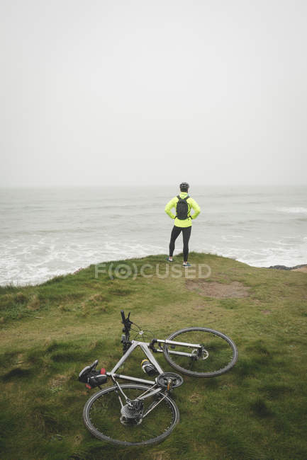Visão traseira do homem em pé na colina na costa do mar — Fotografia de Stock