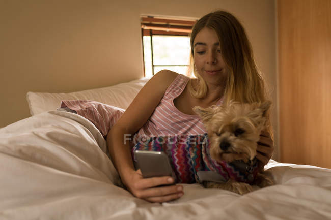 Girl with dog using mobile phone in bedroom at home — Stock Photo