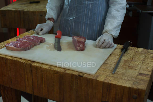 Corte médio de açougueiro de pé com pedaço de carne no açougue — Fotografia de Stock