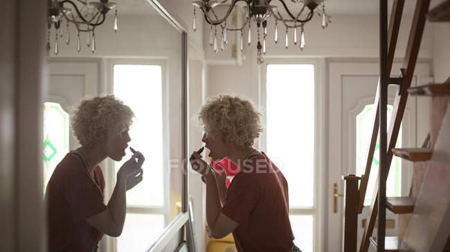 Mujer joven aplicando lápiz labial en casa - foto de stock