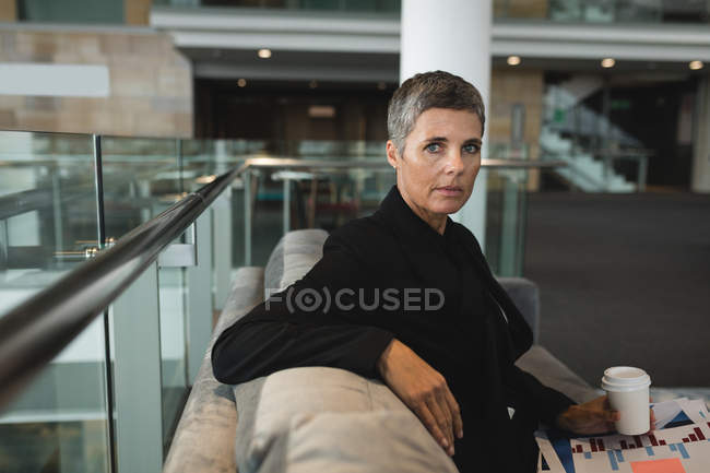 Портрет деловой женщины с чашкой кофе, сидящей на диване в офисе — стоковое фото