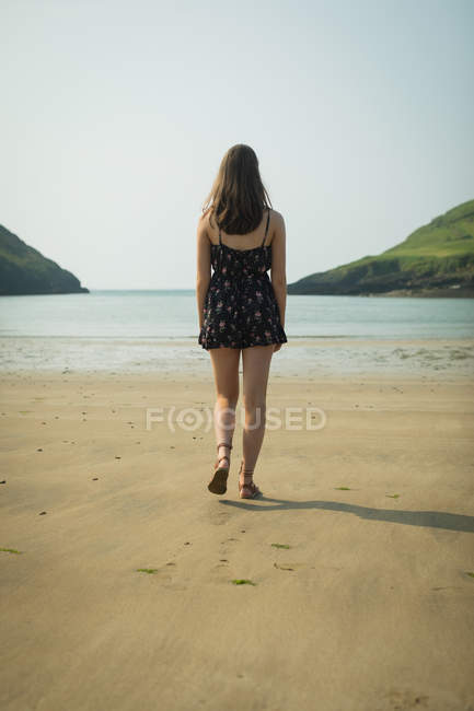 Вид сзади на женщину, идущую по пляжу в солнечный день — стоковое фото