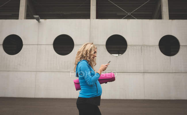 Вид сбоку беременной женщины с помощью мобильного телефона — стоковое фото