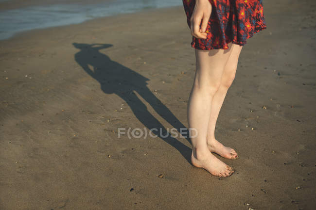 Sección baja de la mujer jugando con su sombra en la playa - foto de stock
