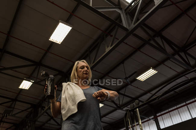 Behinderte ältere Frau überprüft Zeit beim Wassertrinken in der Turnhalle — Stockfoto