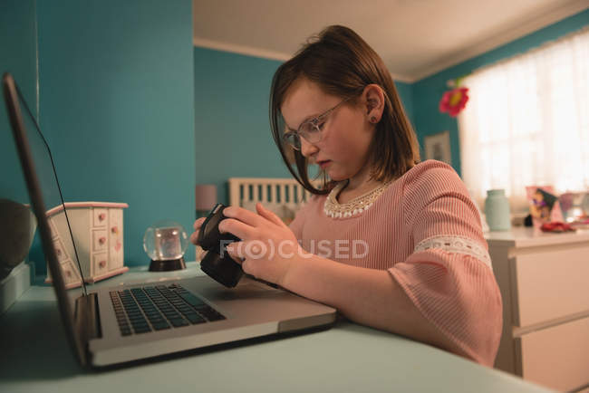 Chica mirando a la cámara mientras usa el ordenador portátil en el dormitorio en casa - foto de stock