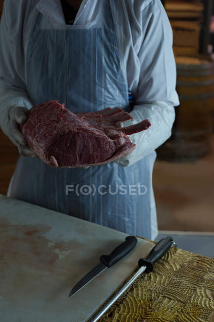 Parte média do açougueiro segurando a carne na mão no açougue — Fotografia de Stock