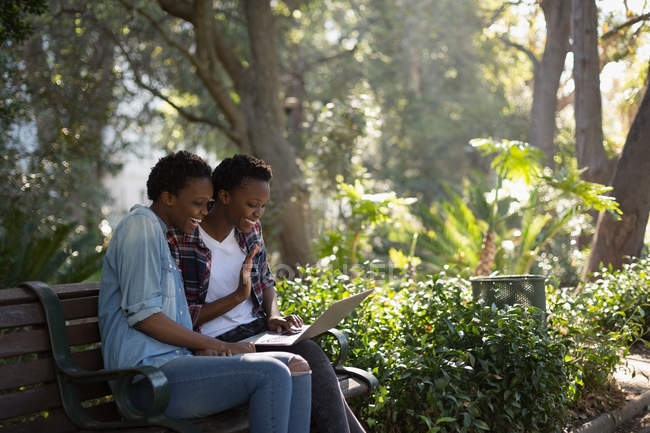 Близнецы используют ноутбук в парке в солнечный день — стоковое фото