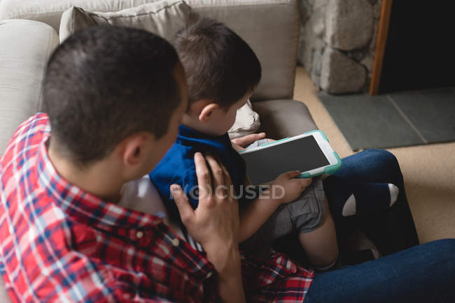 Padre e hijo usando tableta digital en la sala de estar en casa - foto de stock
