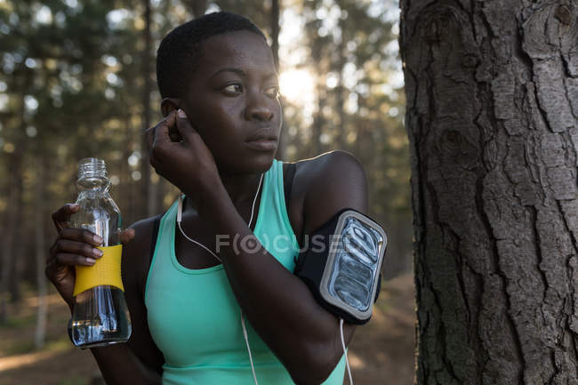 Sportlerin mit Wasserflasche hört Musik im Wald — Stockfoto