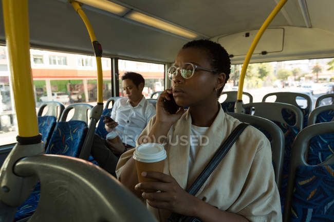Woman talking on mobile phone while having coffee in bus — Stock Photo