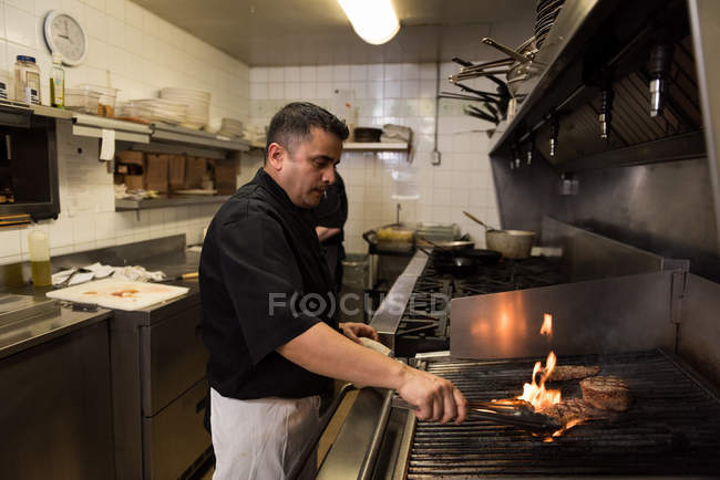 Male chef cooking meat in barbecue at kitchen — Stock Photo