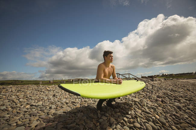 Surfista com prancha agachada em seixos na praia — Fotografia de Stock