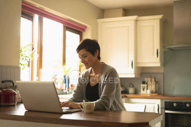 Mujer usando el ordenador portátil en la cocina en casa - foto de stock